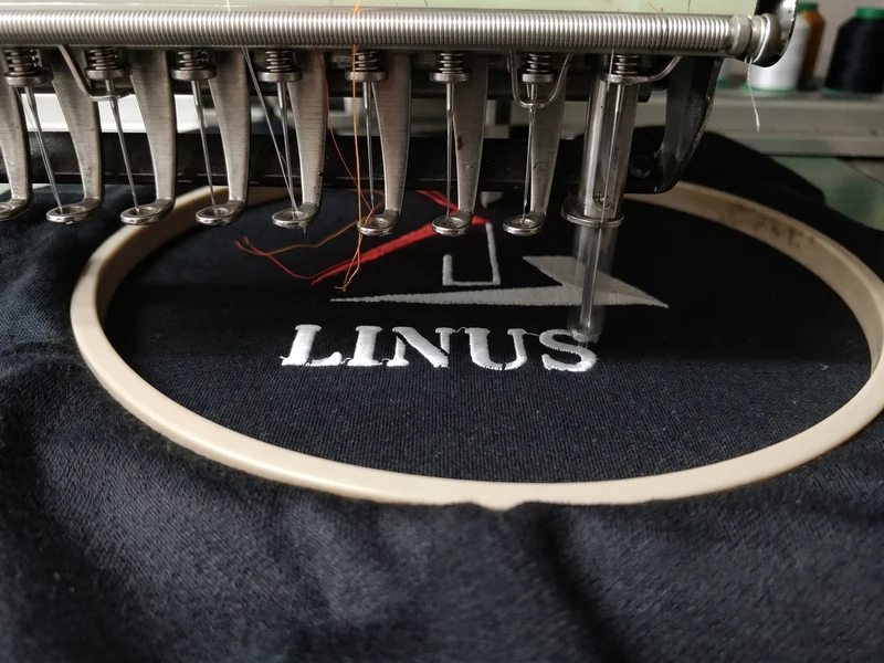 Embroidery service — a multi-needle machine stitching a custom logo onto a dark garment at the Linushi factory